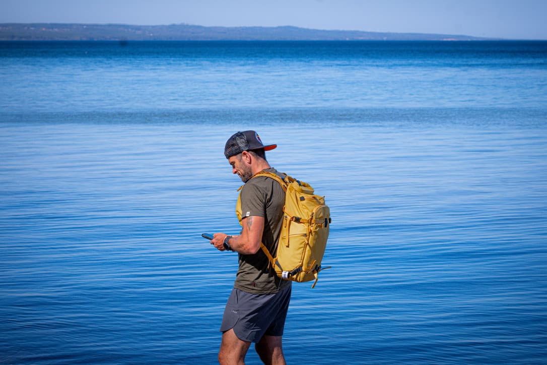 Patrik Widell står vid havet med ryggsäck och mobil i handen.